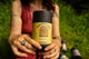 Seated person holding The Soother herbal tea canister labeled Digestive Repair, more canisters lying in the grass