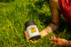 Tattooed hands resting The Dreamer herbal tea canister, labeled Sip Into Slumber, in bright green grass
